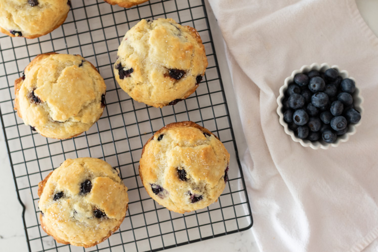 fresh blueberry muffins on rack next to a ramekin of fresh blueberries