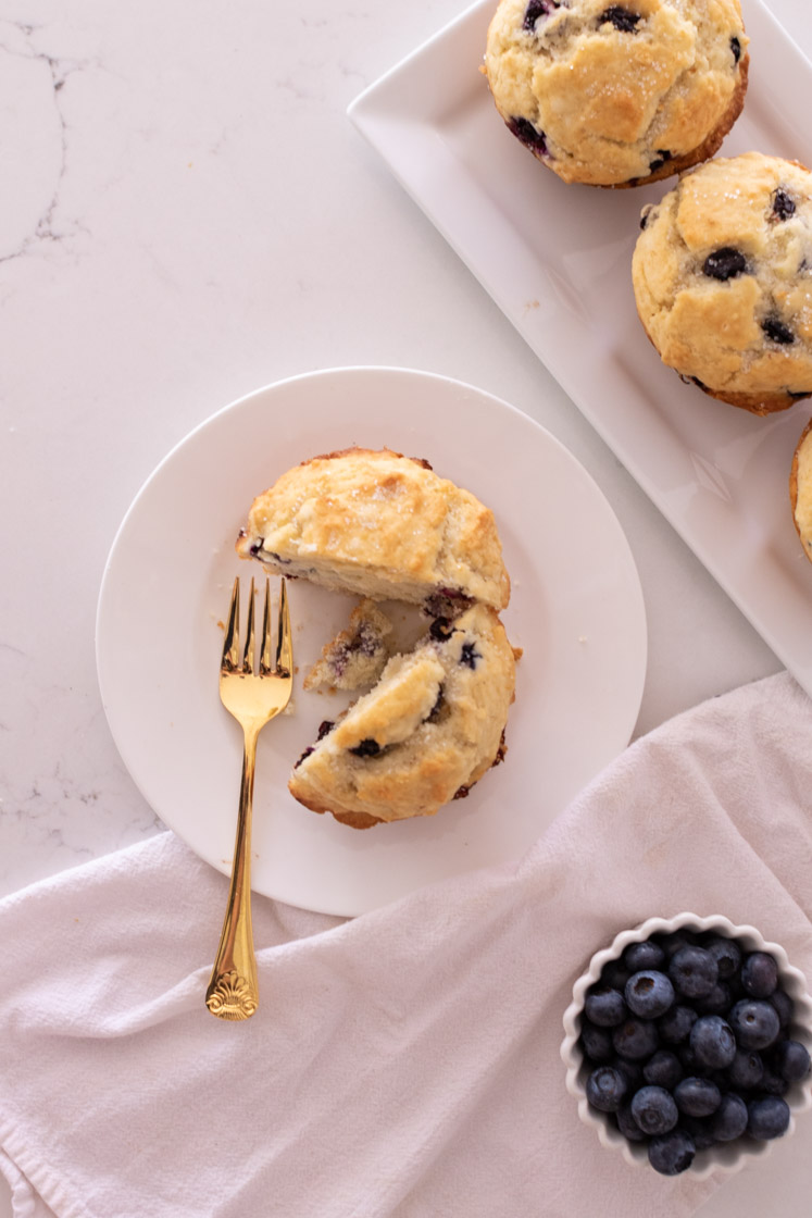 blue berry muffin cut in half on saucer with fork