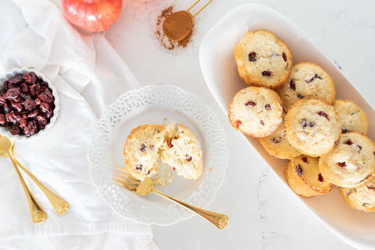 Apple Cranberry muffins in a bowl on table next to a saucer with a cut muffin