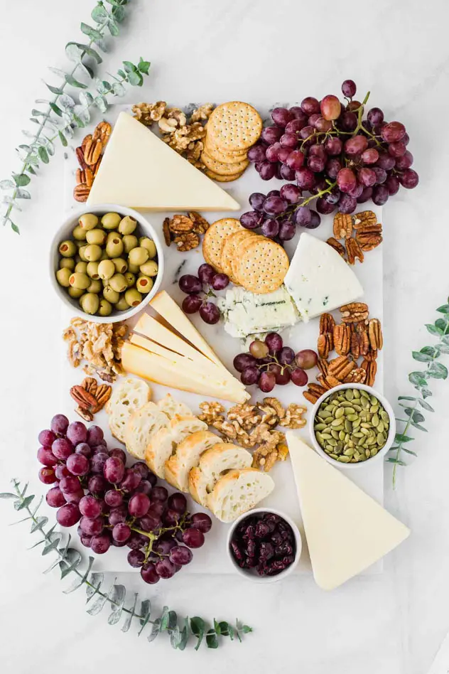 cheese board on marble with grapes, sunflower seeds, cheese, nuts, olives and more